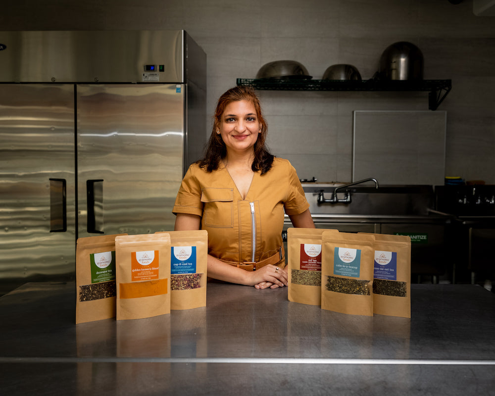 the founder of ayursome foods in a beige dress, with herbal tea and turmeric spice mix at a commercial kitchen