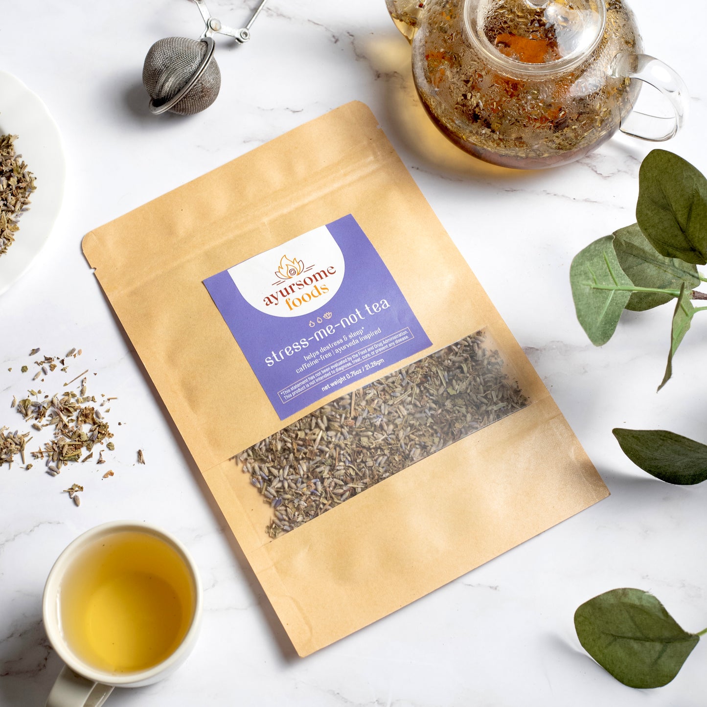 Ayurveda Tea for Stress relief containing Lavender tea and loose leaf Lemon Balm is packed in kraft paper pouch. Next to the tea for anxiety is a cup and pot of the brewed herbal tea and tea accessories