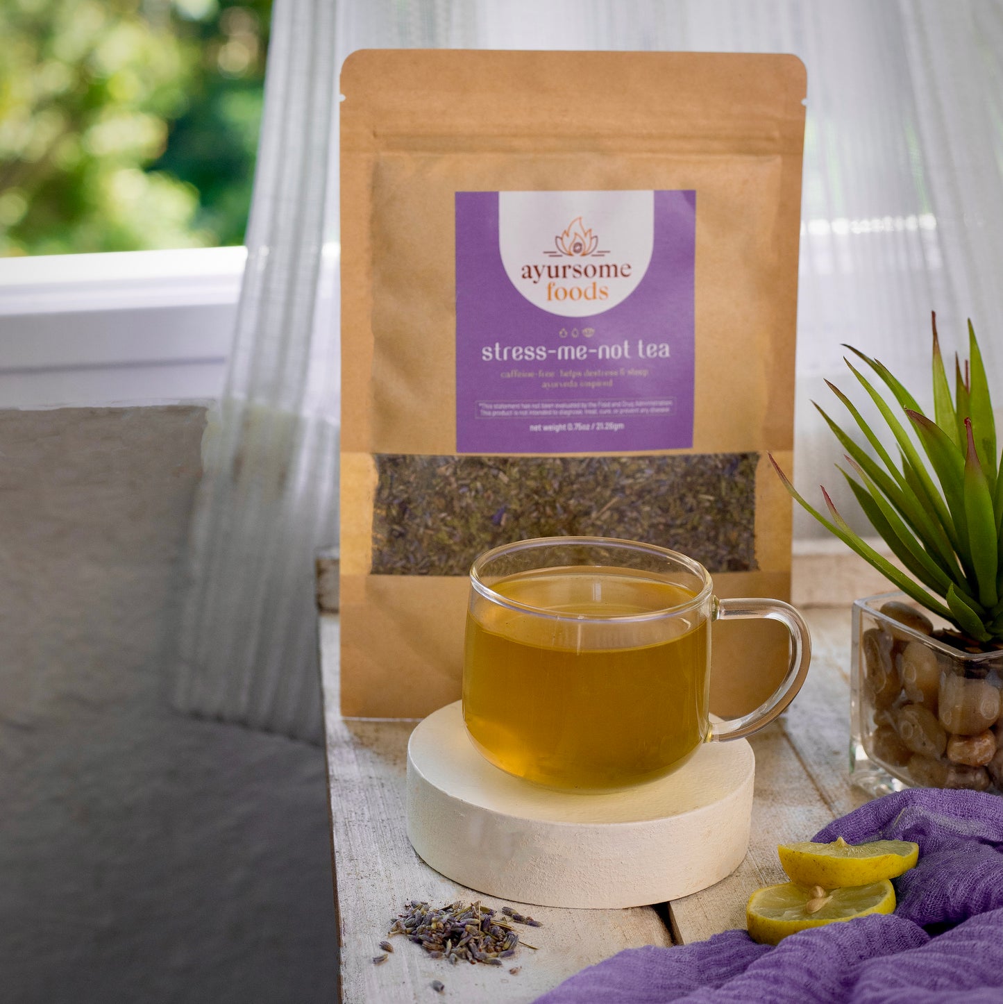 a cup of lavender tea for sleep along with loose leaf tea pack. the shot is against white background with a few slices of lemon and a purple napkin