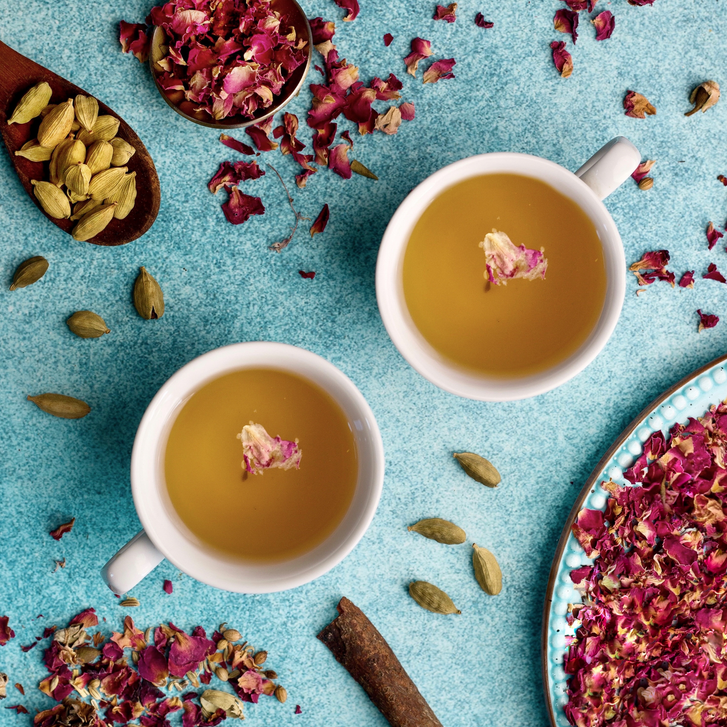 organic ingredients used in ayursome foods' cup it cool tea, including rose, cardamom, licorice root tea. the ingredients and the brewed herbal tea are shot against a soothing blue background